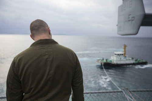 A Marine with the 31st Marine Expeditionary Unit watches as a tug boat guides the USS Bonhomme Richard (LHD 6) out of port at White Beach, Okinawa, Japan, Feb. 6, 2016. The Marines and sailors of the 31st MEU and the Bonhomme Richard Amphibious Ready Group are currently on their spring deployment to the Asia-Pacific region. (U.S. Marine Corps photo by Gunnery Sgt. Zachary Dyer/Released)