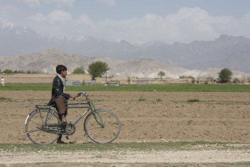 An Afghan boy stops on his bike in Khanjar Khel, Parwan Province, Afghanistan, to watch as U.S. Army Explosive Ordnance Disposal technicians secure the site of a crashed F-16 Fighting Falcon from Bagram Airfield, Afghanistan. The F-16 crashed after takeoff and the pilot safely ejected; since then, the base completed cleaning up the crash site. The cause of the accident is under investigation. (U.S. Air Force photo/Tech. Sgt. Robert Cloys)