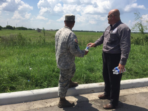 Judge Blake Sylvia, Chambers County Justice of the Peace, right, hands cold water to a Texas Guardsman, September 1, 2016, in Wallisville, Texas. Texas Army National Guard maintenance soldiers from the 1st Battalion, 149th Aviation Regiment (Attack Reconnaissance) waded through six-inch deep mud and worked in a heat index of more than 100 degrees, to prepare an AH-64D Apache helicopter for recovery operations using a CH-47 Chinook helicopter, following a precautionary landing in a rice paddy. (U.S. Army National Guard photo by Capt. Martha Nigrelle)