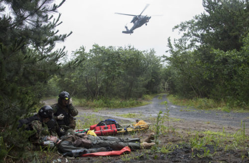 Two Japan Air Self-Defense Force pararescuemen from Akita Air Base, Japan, respond to a simulated downed pilot as a UH-60J Black Hawk flies overhead during exercise Cope Angel 17 at Draughon Range near Misawa Air Base, Japan, Aug. 9, 2017. All pilots are equipped with survival equipment for situations they would have to eject from their aircraft and wait to be rescued. The equipment includes life-saving survival equipment capable for use during an ejection and waiting for rescue. (U.S. Air Force photo by Airman 1st Class Sadie Colbert)